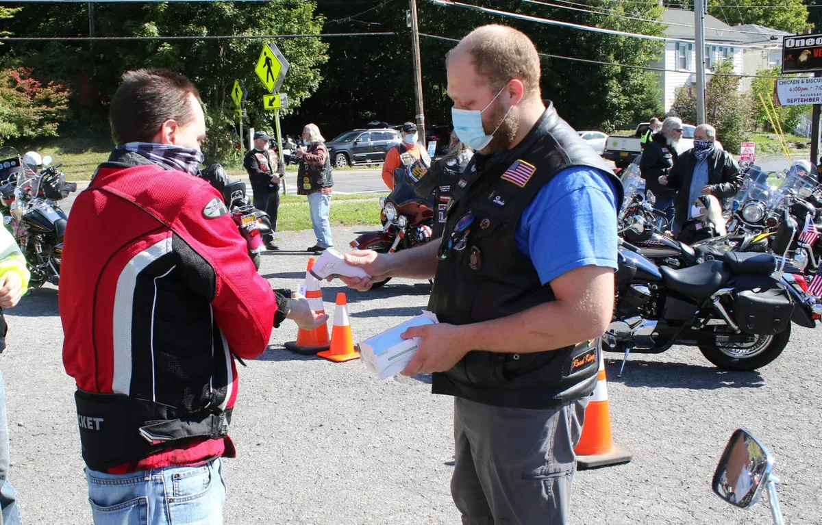 Two volunteers wearing masks and discussing registration at an outdoor motorcycle event