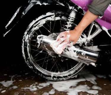 A hand washing a motorcycle wheel with a soapy sponge