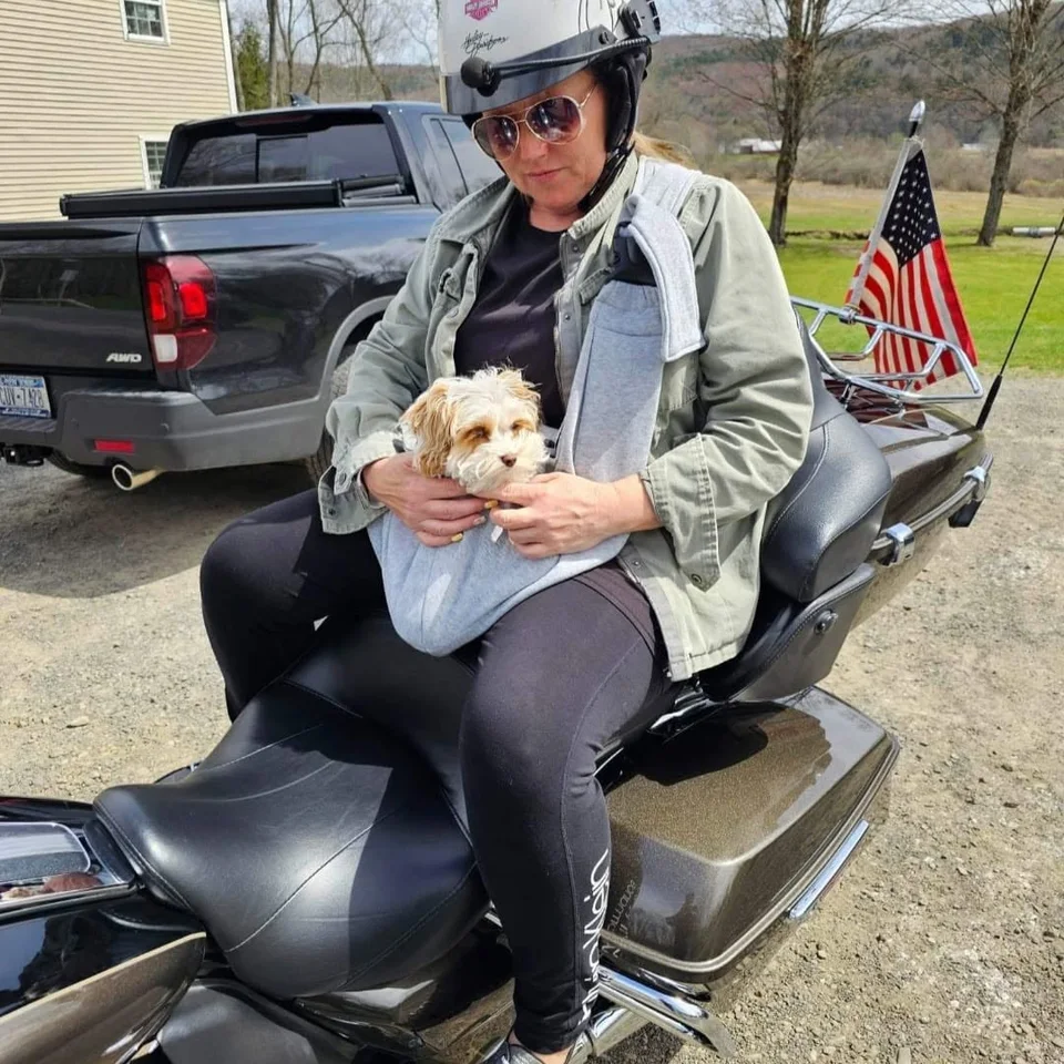 Deb Dennis wearing a motorcycle helmet and holding Bailey on a Harley-Davidson