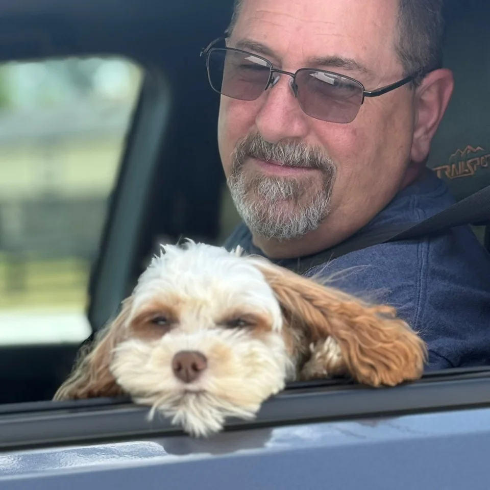 Bailey resting her head on a car window beside Chris Dennis