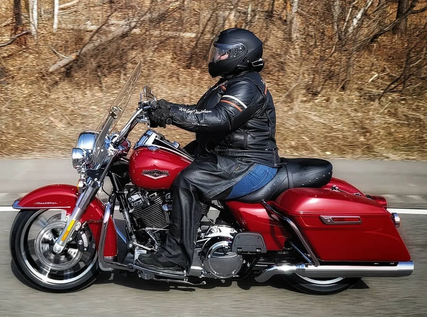 Charlotte Chase riding Stella, her cherry-red Harley-Davidson, along a country road in full leathers and a black helmet