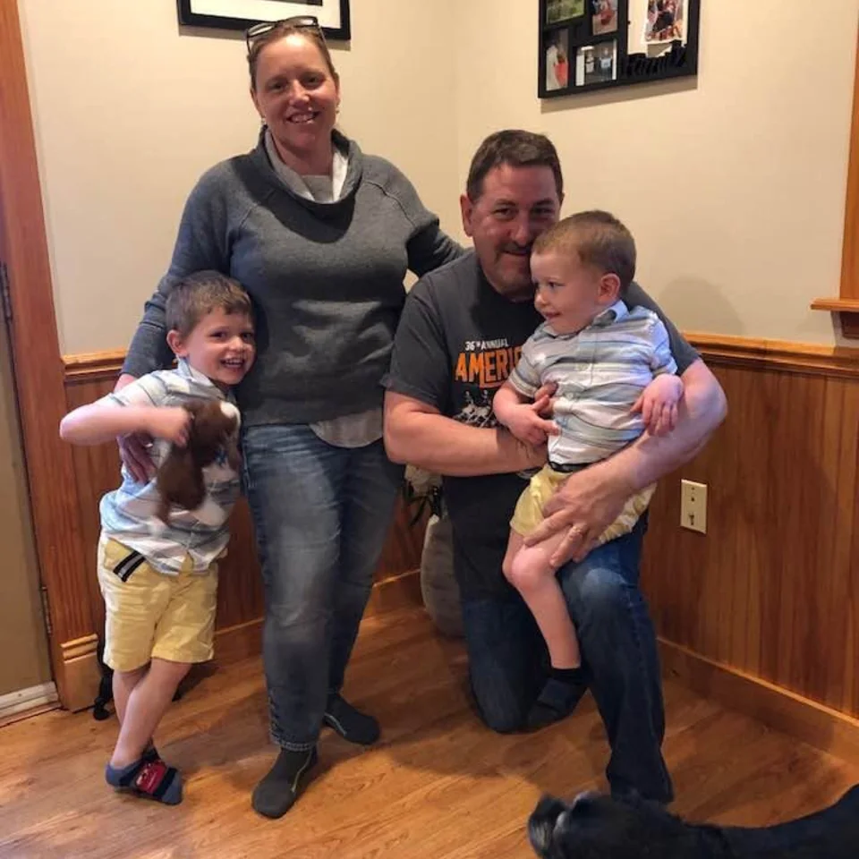 Chris and Deb Dennis indoors with two young children and a black dog