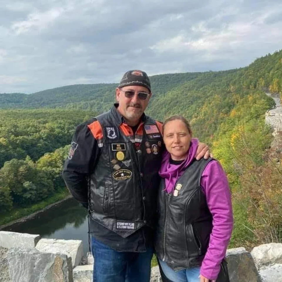 Chris and Deb Dennis in riding gear at a scenic river overlook