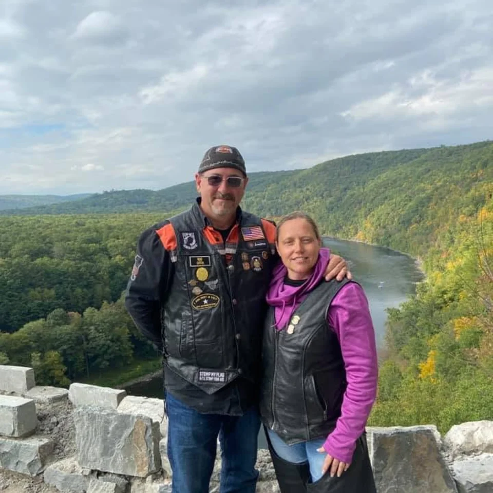 Chris and Deb Dennis in riding gear at a scenic overlook above a river