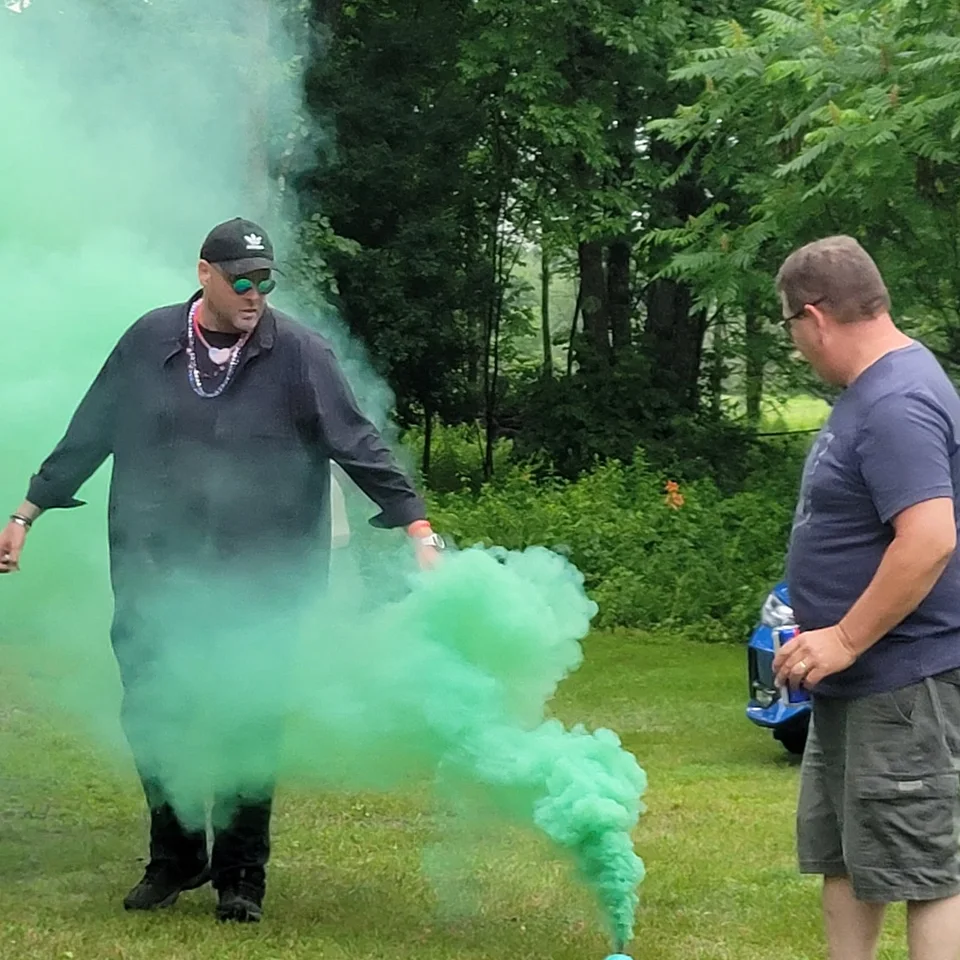Chris Dennis standing beside green smoke at an outdoor gathering