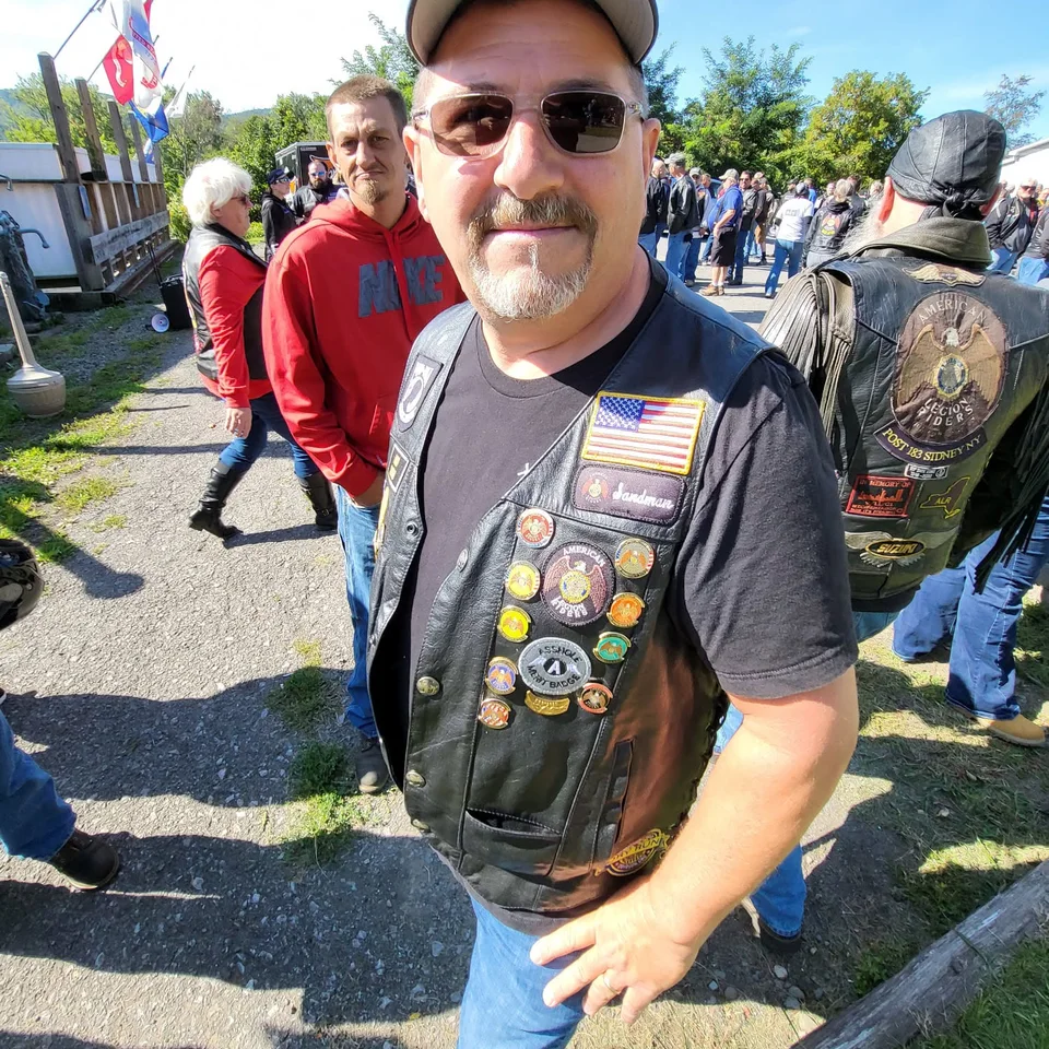 Chris Dennis smiling in his American Legion Riders vest at an outdoor gathering