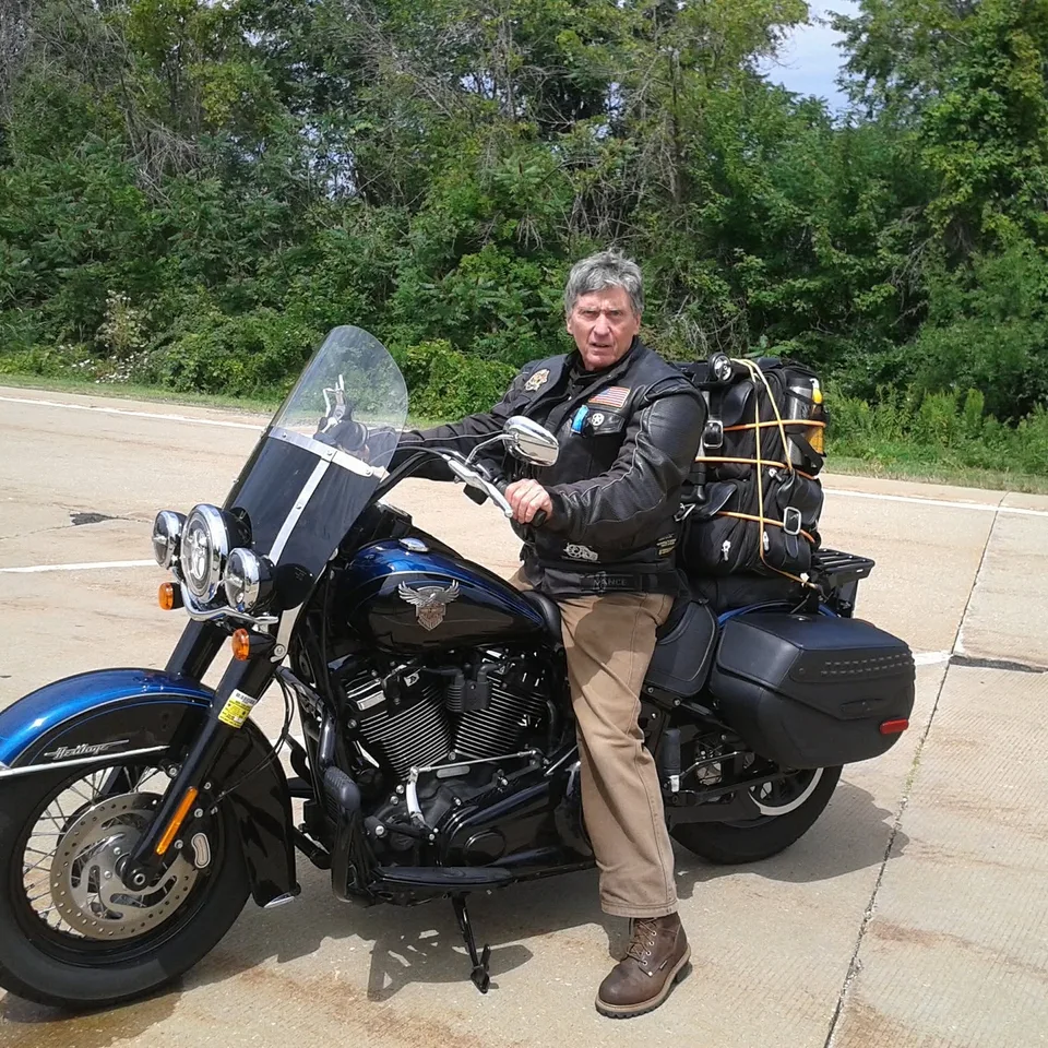 David Buck sitting on a blue Harley-Davidson Heritage loaded for travel