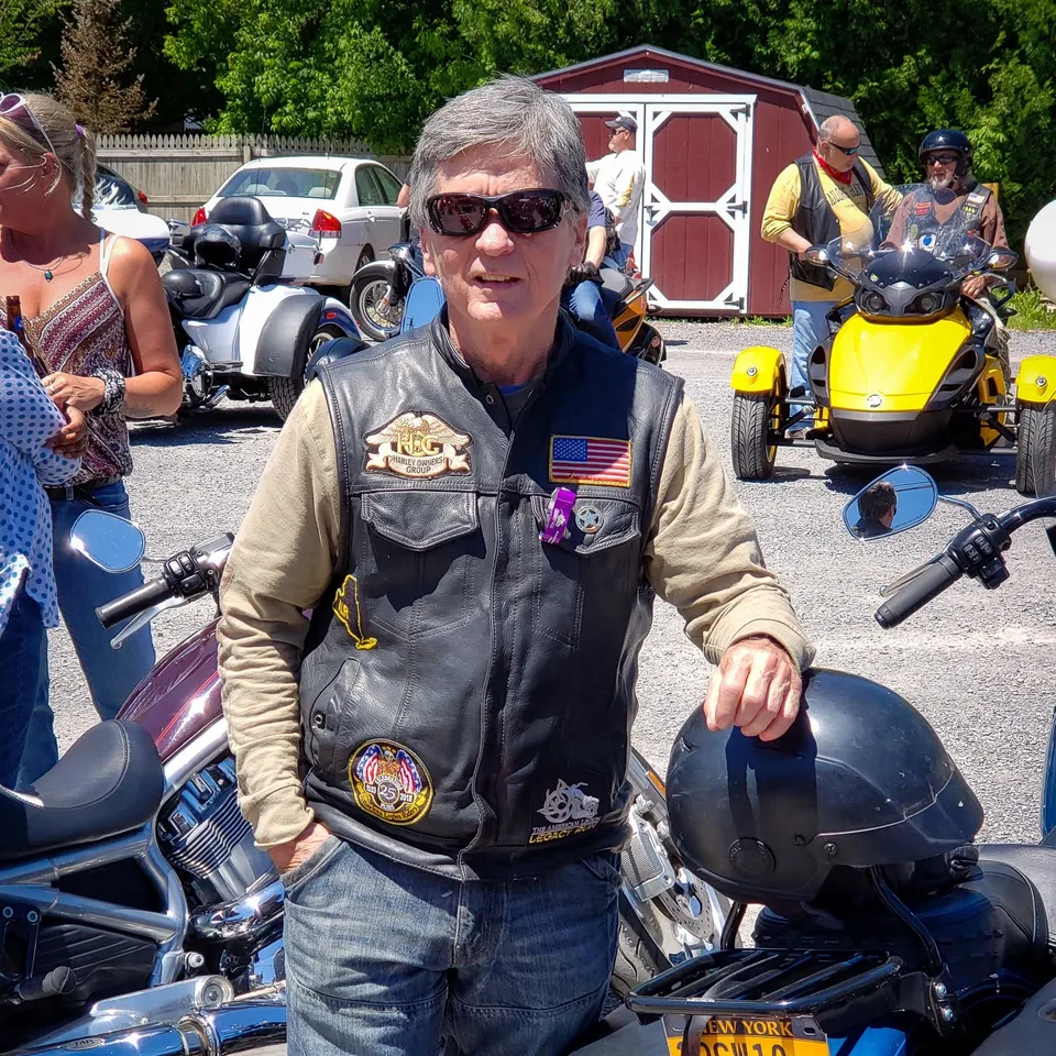 David Buck wearing sunglasses and his leather vest beside motorcycles