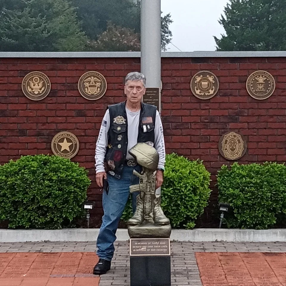 David Buck standing beside a kneeling soldier statue at a military memorial