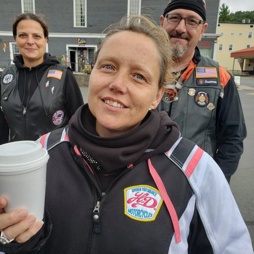 Deb Dennis holding a cup with two fellow riders at an outdoor gathering