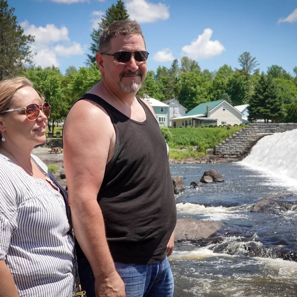 Deb and Chris Dennis standing beside a waterfall on a sunny day