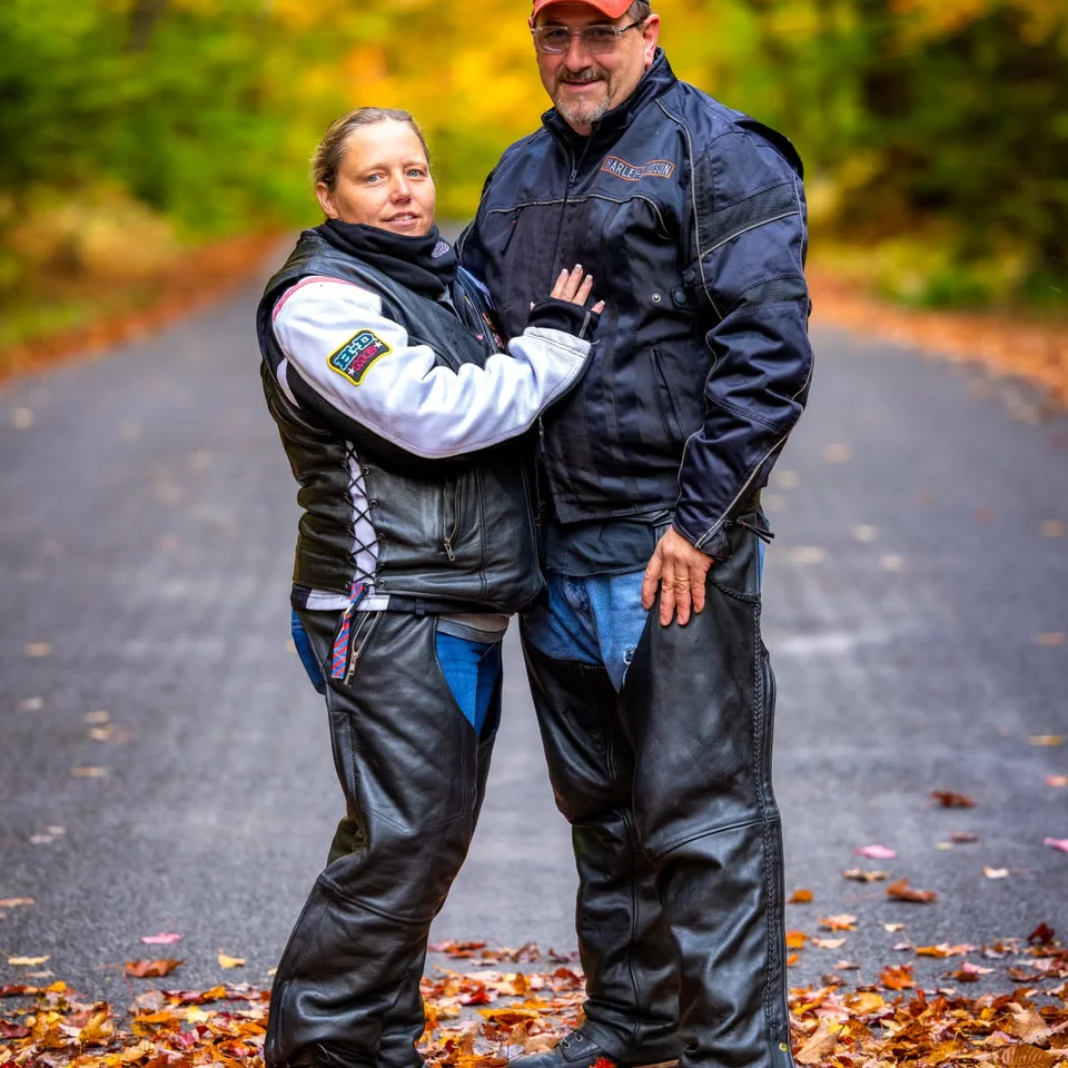 Deb and Chris Dennis embracing on a wooded road in autumn