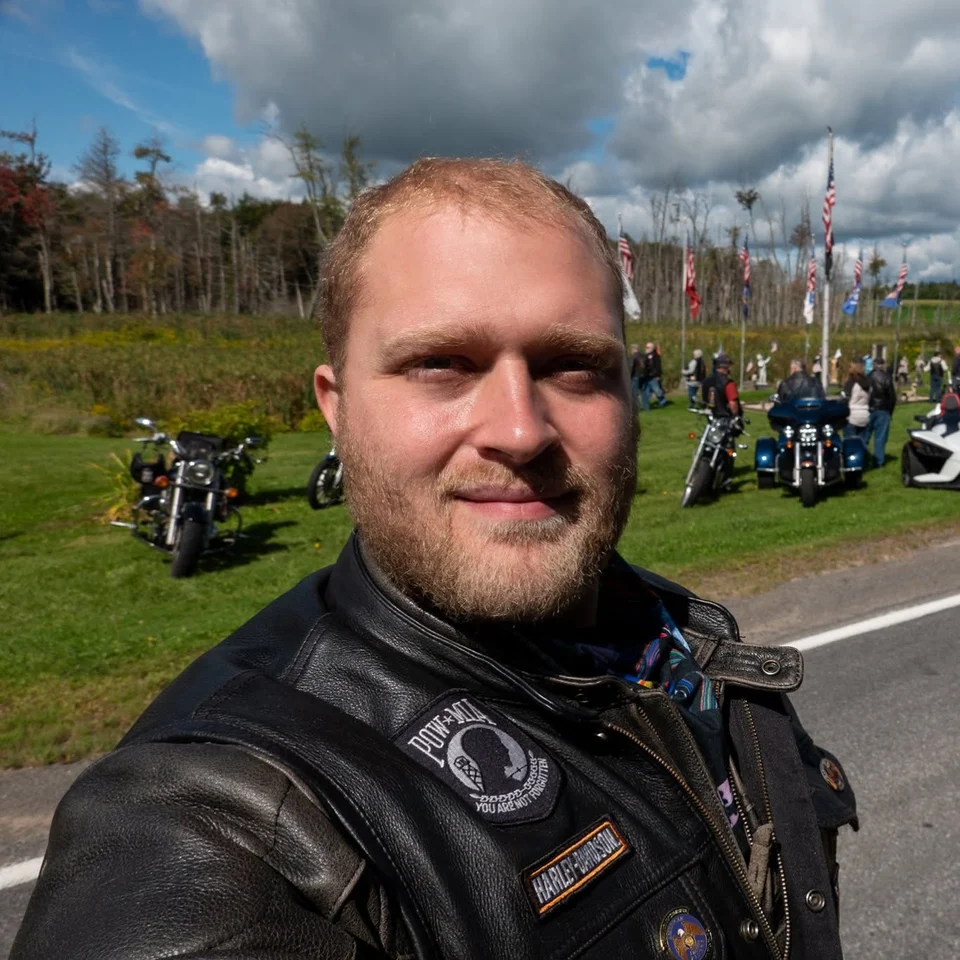 Devin Chase in his riding vest with motorcycles and American flags behind him