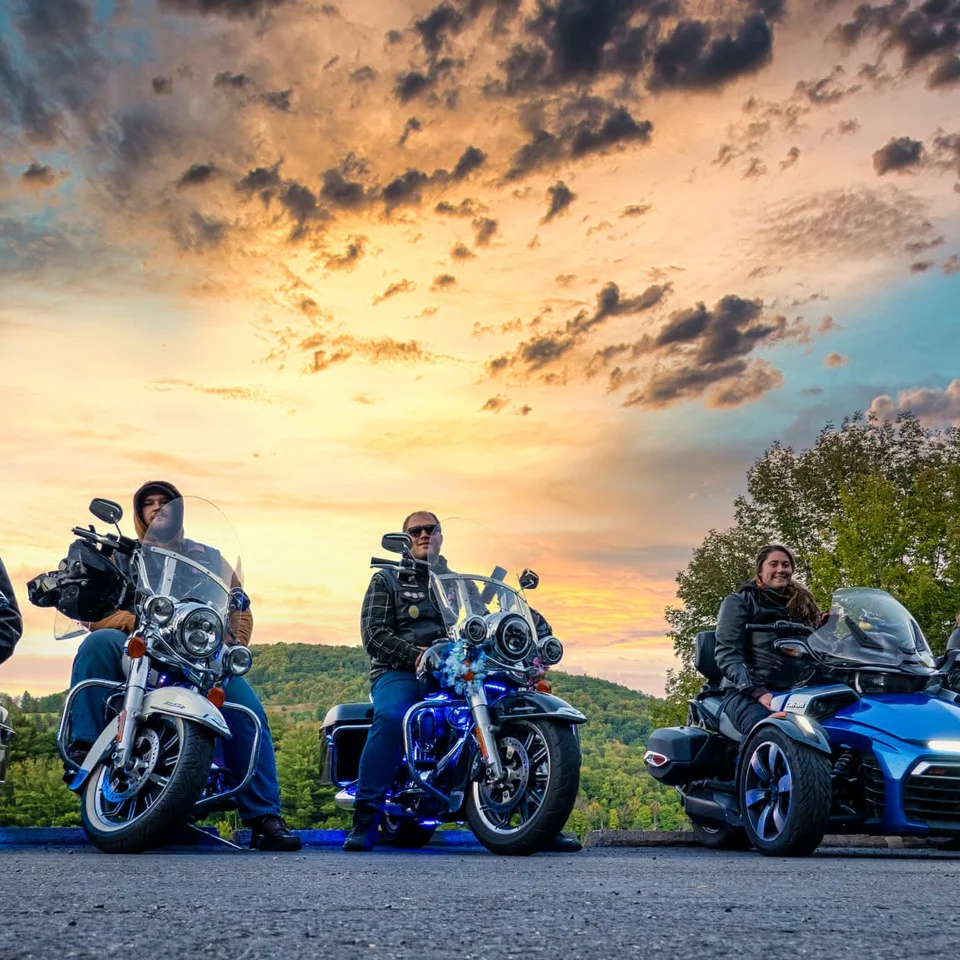 Five riders lined up with their motorcycles beneath a colorful sunset