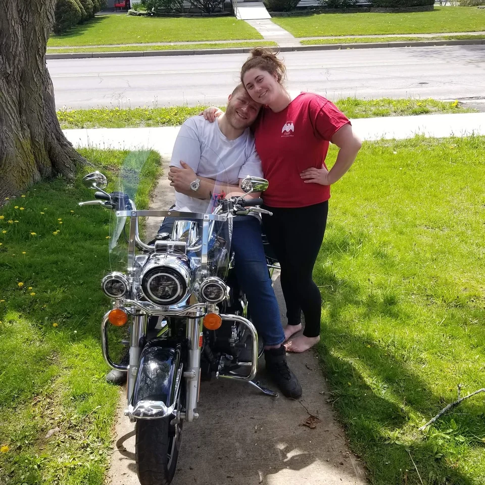 Devin Chase seated on a motorcycle with Rebecca Chase standing beside him