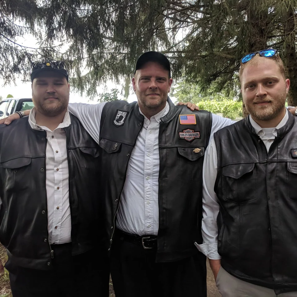 Dillon Chase standing outdoors with Chris Chase and Devin Chase in their riding vests
