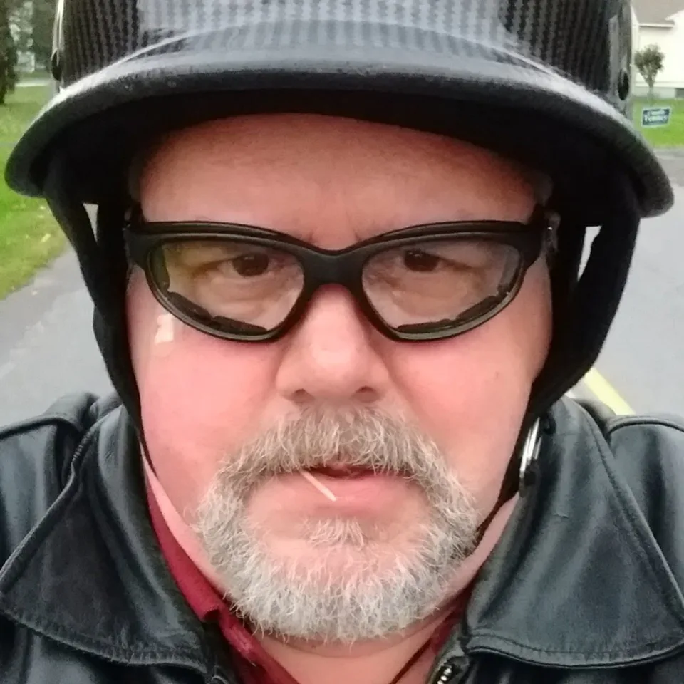 John Creaser wearing a motorcycle helmet, riding glasses, and a leather jacket
