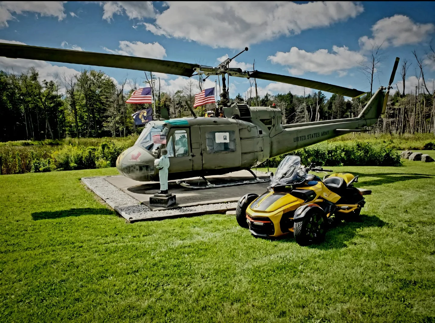 Rob Martinez’s yellow Can-Am Spyder parked on the grass beside a U.S. Army Huey helicopter flying American flags