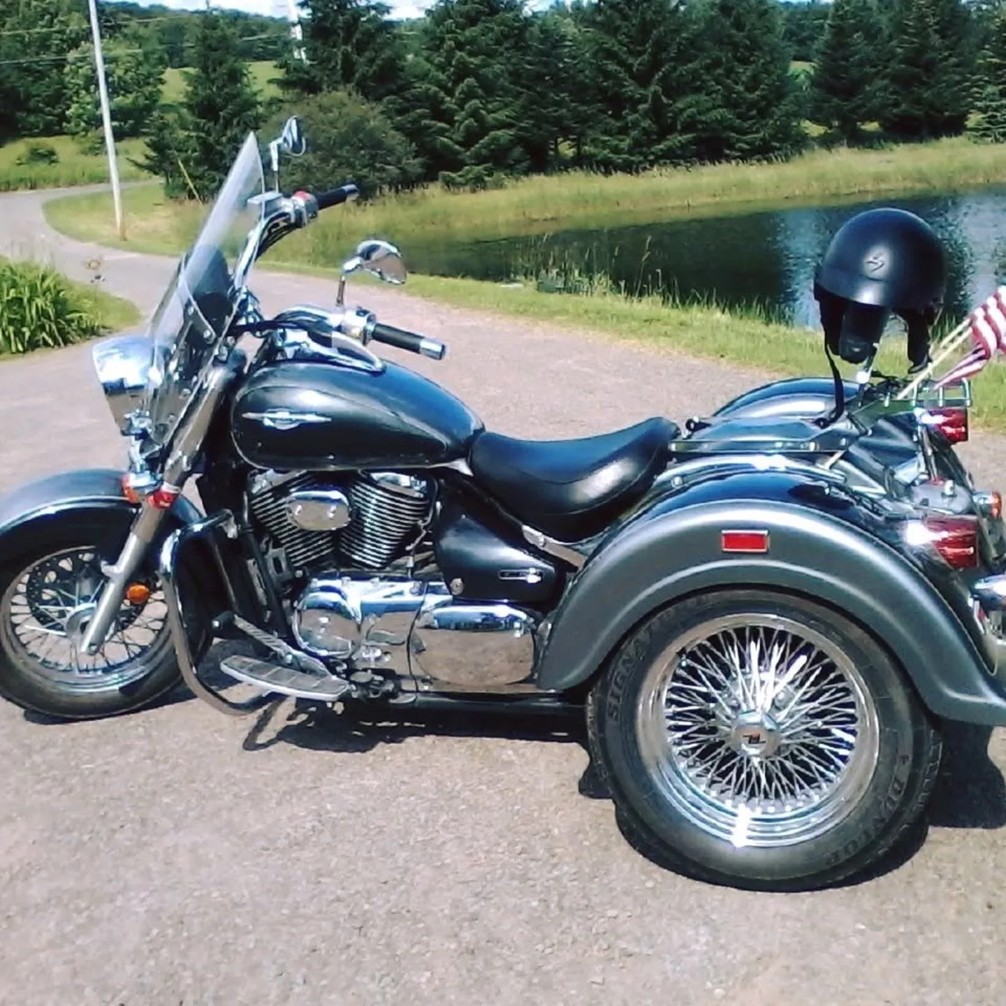 Sharon Parshall’s black Suzuki trike with spoked rear wheels and an American flag, parked by a pond