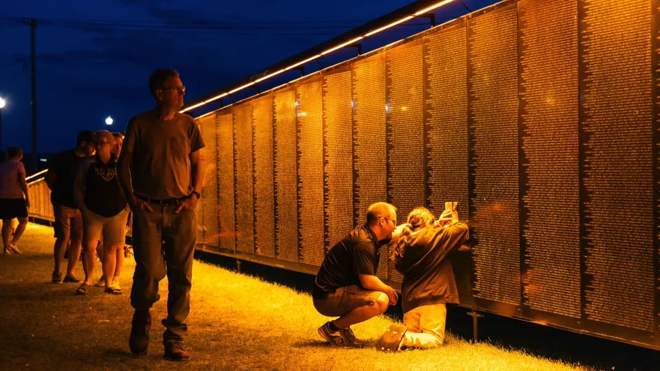 Visitors find names on The Wall That Heals at night under amber lights