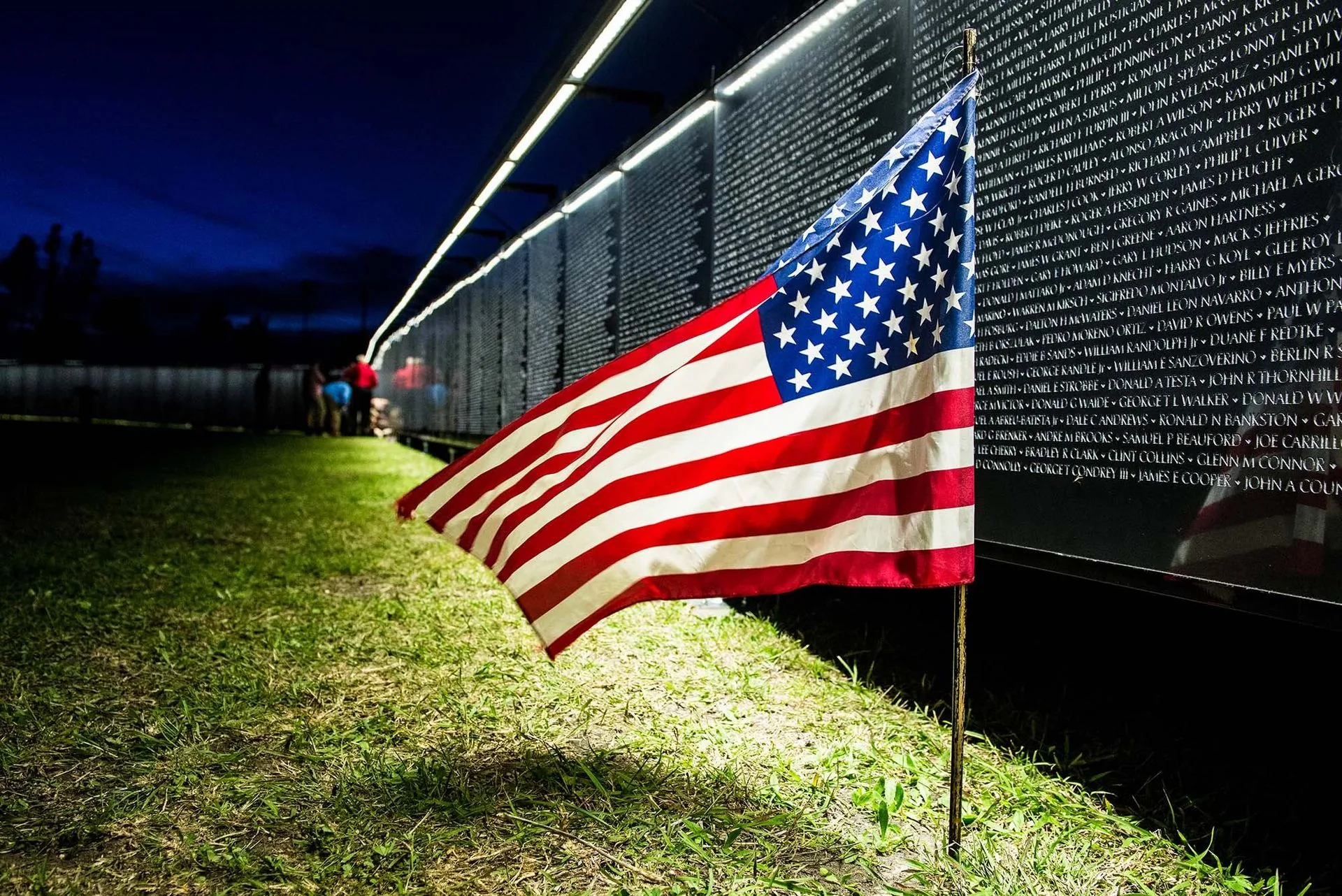 An American flag stands beside a panel of The Wall That Heals at night