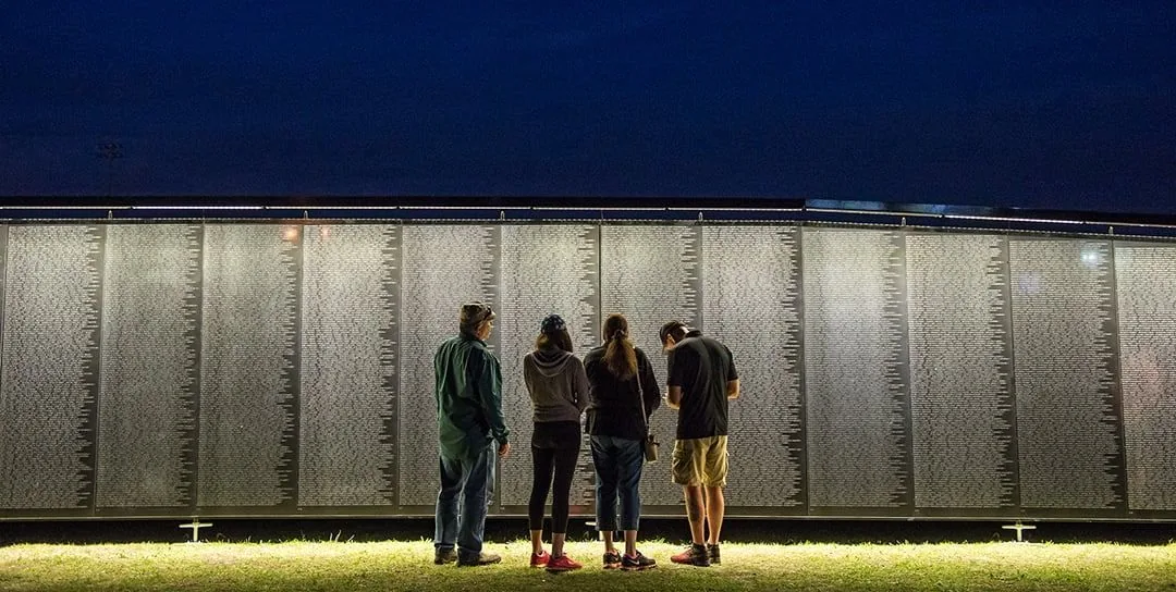 Four visitors stand together at The Wall That Heals at night