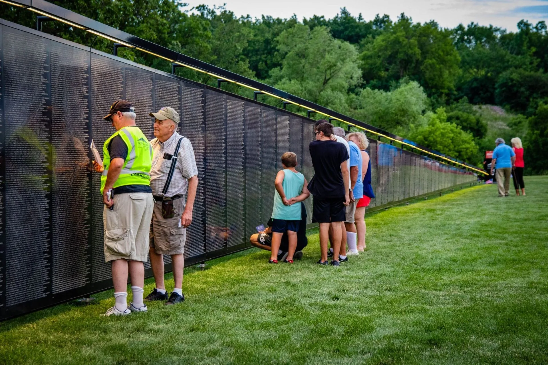 A volunteer in a yellow vest helps a visitor locate a name on The Wall